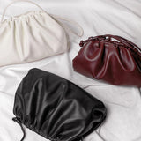 Drie Serena Zachte Leren Pouch Tassen van Liora The Label in wit, bordeauxrood en zwart worden getoond op zachte witte stof. Ze hebben elk een gerimpeld ontwerp en een dun koordje voor een moderne, minimalistische look.