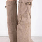 Een persoon draagt Liora The Label Dames Kniehoog Laarzen met Brede Flare Bovenkant en Blokhak, staande op een licht houten vloer tegen een witte achtergrond.