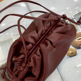 De Serena Zachte Leren Pouch Tas van Liora The Label - minimalistisch, modern en soepel - met verzamelde details, ligt op een open magazine met geweven ronde krukken in het ontwerp.