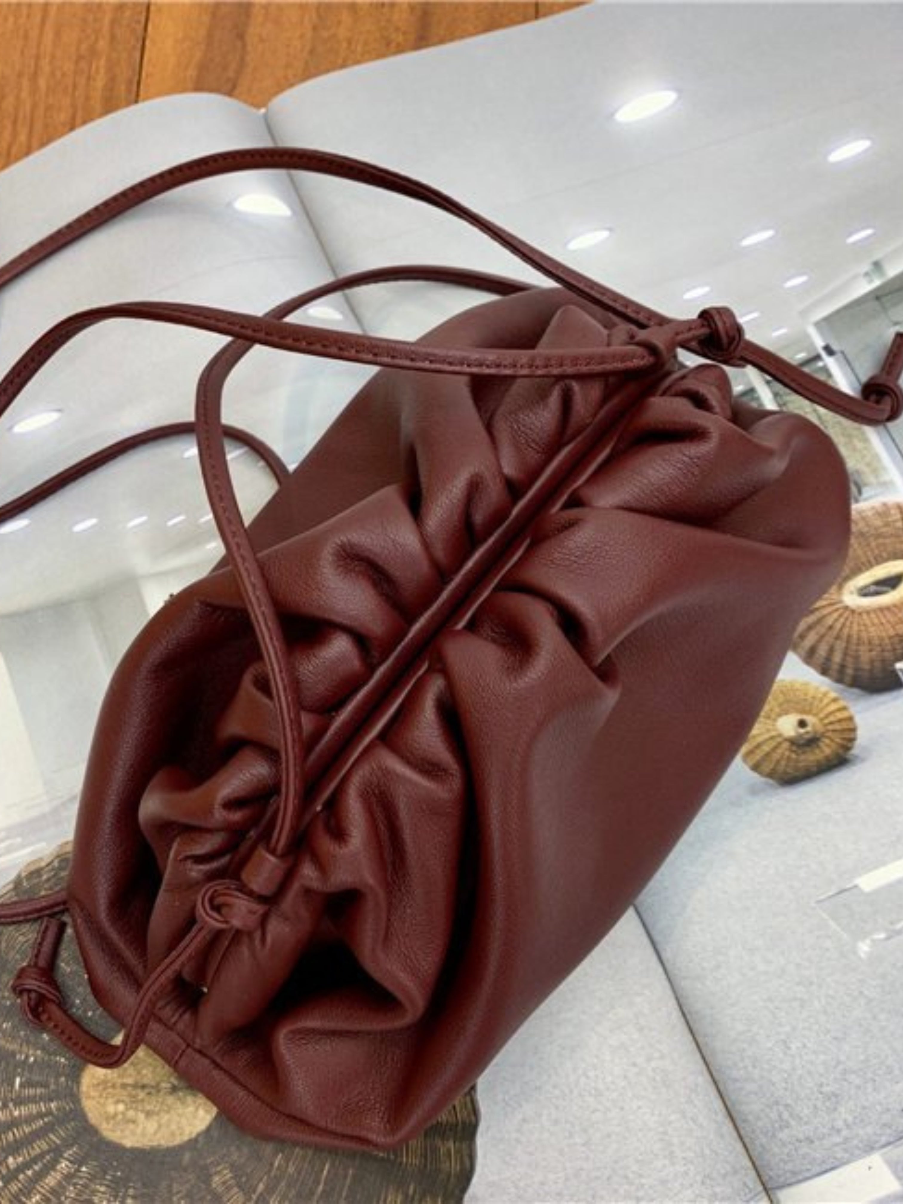 De Serena Zachte Leren Pouch Tas van Liora The Label - minimalistisch, modern en soepel - met verzamelde details, ligt op een open magazine met geweven ronde krukken in het ontwerp.