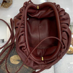 De Serena Zachte Leren Pouch Tas van Liora The Label, een kastanjebruin minimalistisch leren tasje met gouden accenten, ligt open op een tijdschrift op een houten oppervlak, met een zonnebril zichtbaar in de linkerbovenhoek.