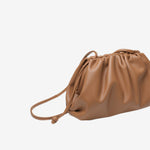 De Serena Zachte Leren Pouch Tas van Liora The Label is een bruine, geruwde leren schoudertas met een lange dunne riem en een minimalistisch ontwerp, afgebeeld tegen een witte achtergrond.