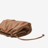 De Serena Zachte Leren Pouch Tas van Liora The Label is een minimalistische, moderne bruine clutch van boterzacht leer met een geplooid ontwerp en trekkoordsluiting, stijlvol gepresenteerd op een witte achtergrond.