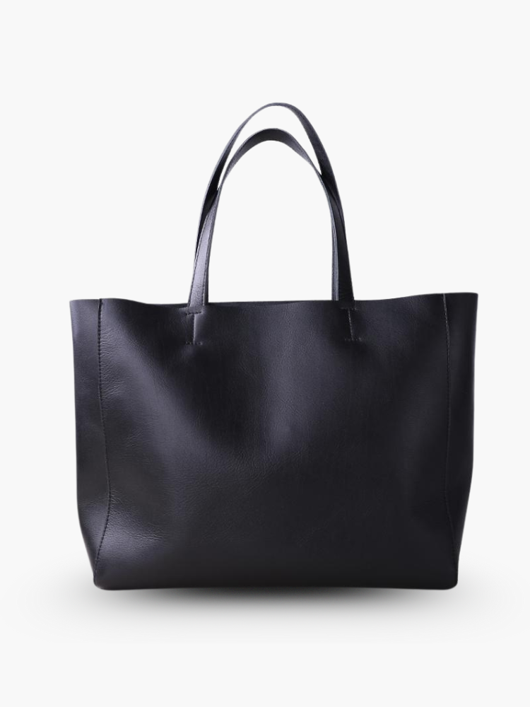 De Emma zwarte leren tote bag van Liora The Label is een ruime en veelzijdige handtas met twee hengsels, gemaakt van echt leer en stijlvol rechtopstaand tegen een witte achtergrond.