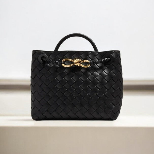 De Alyn zwarte geweven midi leren tote bag van Liora The Label, met korte handgreep en goudkleurige sluiting, straalt moeiteloze elegantie en tijdloze aantrekkingskracht uit. Perfect als luxe handtas voor dames, gepresenteerd tegen een lichte achtergrond.