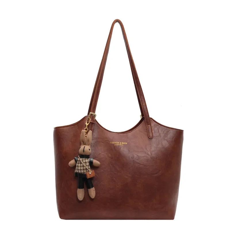 De Thalessa Chic Leren Tote Bag met Speelse Charme van Liora The Label heeft twee schouderbanden en wordt geleverd met een pluche konijnen sleutelhanger in geruite outfit, speels hangend aan één van de handvatten.