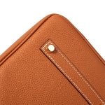 Close-up van de Isla Tan Textured Leather Handtas van Liora The Label, met bruin structuurleer, witte stiksels en een gouden klinknagel detail - tijdloos ontwerp van Klassiek & Tijdloos.