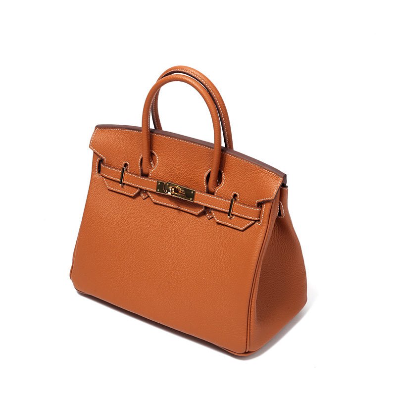 De Isla Tan Textured Leather Handtas van Liora The Label heeft een gestructureerde vorm, dubbele handgrepen en een gouden gesp aan de voorkant, tegen een witte achtergrond.