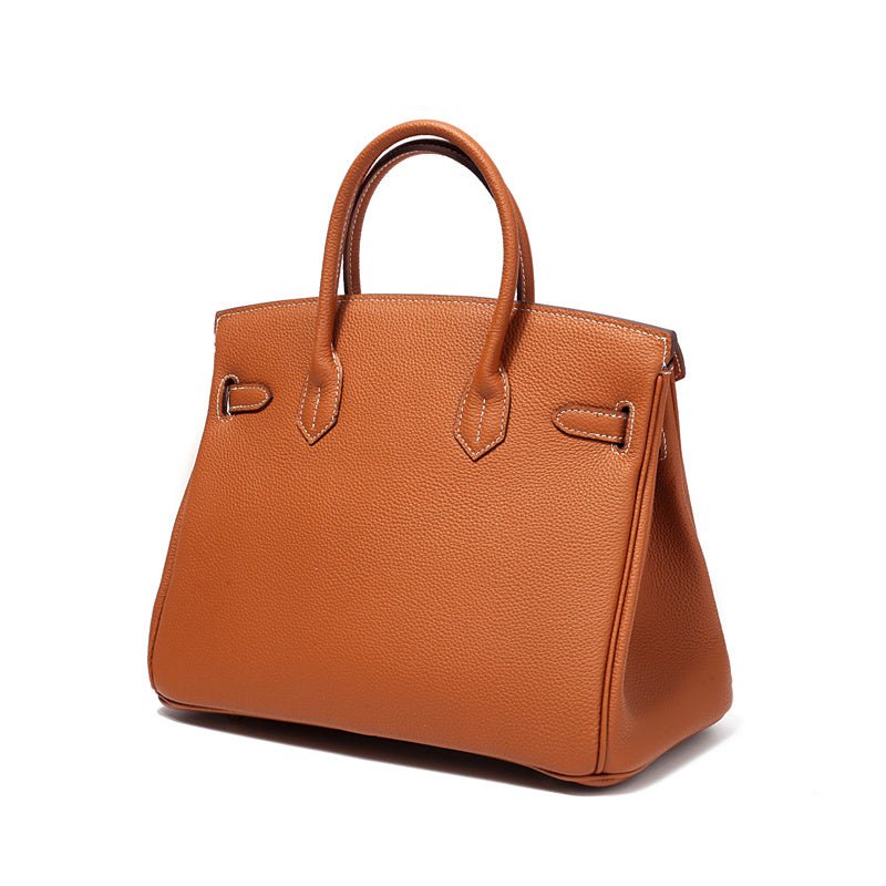 De Isla Tan Textured Leather Handtas van Liora The Label heeft gestructureerde zijkanten, twee handvatten en minimale hardware, uitgevoerd in bruin leer tegen een effen witte achtergrond.