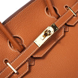 Close-up van de Isla Tan Textured Leather Handtas van Liora The Label, met witte stiksels en een goudkleurig slot op de klepsluiting.