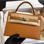 Een hand in een zwarte handschoen houdt de Galatea Elegante Zwarte Leren Handtas van Liora The Label vast, met gouden hardware en gedeeltelijk verpakt in beschermend vilt, in een open doos met wit vloeipapier.