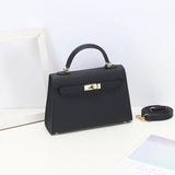 De Aurora Signature Mini Leren Handtas van Liora The Label - een zwarte, gestructureerde tas met bovenhandgreep, gouden hardware en een afneembare schouderriem - rust op een wit oppervlak naast een lege lijst en een pastelkleurig blad.