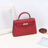 De Aurora Signature Mini Leren Handtas van Liora The Label is een gestructureerde top handtas van volnerf leer met een gouden sluiting en afneembare schouderriem, gepresenteerd op een witte ondergrond naast een wit frame en deels zichtbaar papier.