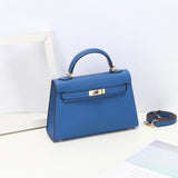 De Aurora Signature Mini Leren Handtas van Liora The Label, een gestructureerde blauwe minitas in volnerf leer met een bovenhandvat en gouden hardware, staat op een wit vlak met de bijpassende schouderriem ernaast.