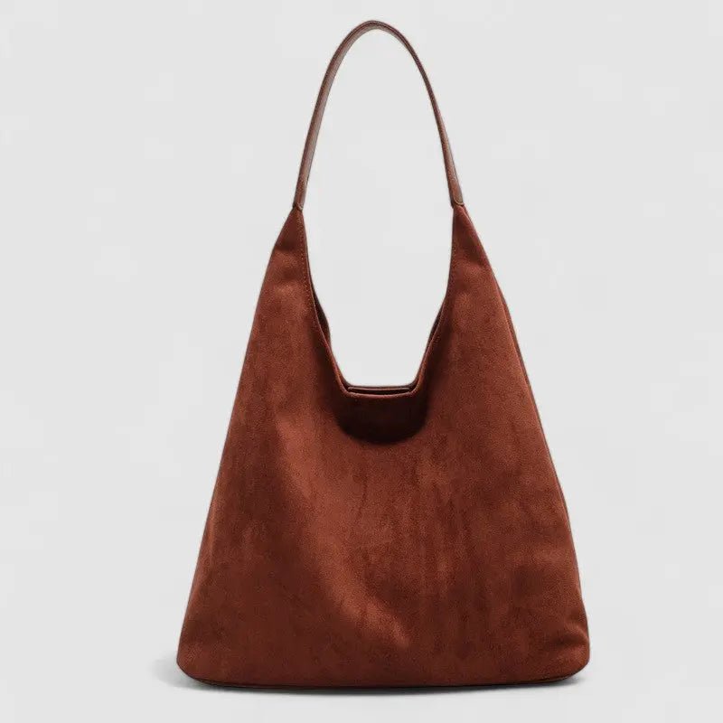 De Lena van Liora The Label is een minimalistische suède hobo tas in warm bruin met één brede schouderband en een soepel, elegant slouchy design, gepresenteerd tegen een lichtgrijze achtergrond.