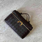 De Luxe Geweven Box Bag van Liora The Label is een elegante donkerbruine crossbody met gouden ritssluiting, getoond op een licht getextureerd oppervlak.