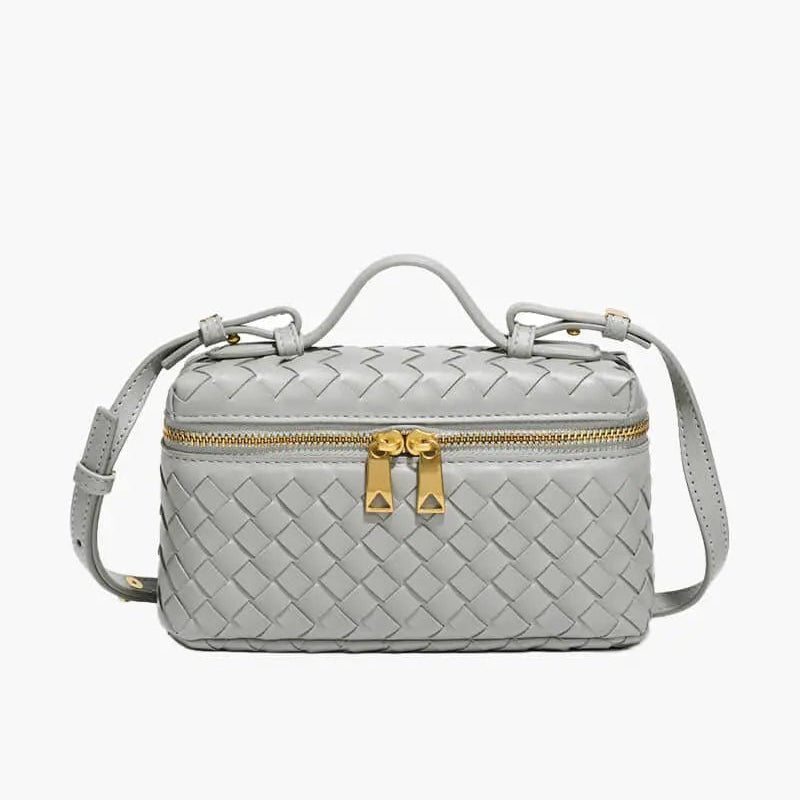 De Luxe Geweven Box Bag van Liora The Label is een kleine, rechthoekige, donkerbruine crossbody van veganistisch leer met gouden ritssluiting, gouden hardware, handvat aan de bovenkant en verstelbare schouderriem.