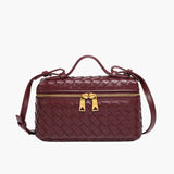 De Luxe Geweven Box Bag van Liora The Label is een elegante donkerbruine crossbody met een gouden ritssluiting, bovenhandgreep en verstelbare schouderriem, afgebeeld op een witte achtergrond.